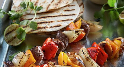 Meat and vegetable kabobs grilled on skewers, on a tray with grilled soft tortillas and salsa