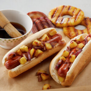 Two grilled hotdogs in buns topped with bits of grilled onion and pineapple
