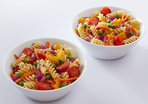 Two bowls of pasta salad, with fusilli, cherry tomatoes, carrots and other fresh vegetables