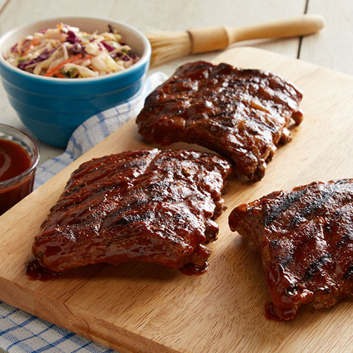 Grilled baby back ribs on a wooden cutting board with a side of coleslaw